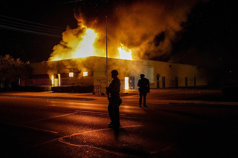 Photo by Morry Gash of The Associated Press / Police stand near a department of corrections building that was on fire during protests, Monday, Aug. 24, 2020, in Kenosha, Wisconsin, sparked by the shooting of Jacob Blake by a Kenosha Police officer a day earlier.