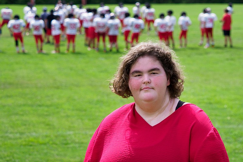 Staff photo by C.B. Schmelter / Signal Mountain student Grace Hammond, shown with the Eagles practicing football in the background Wednesday, is a major supporter of the school's sports teams, with senior lineman Nate Menzel noting she is "really positive no matter what happens."