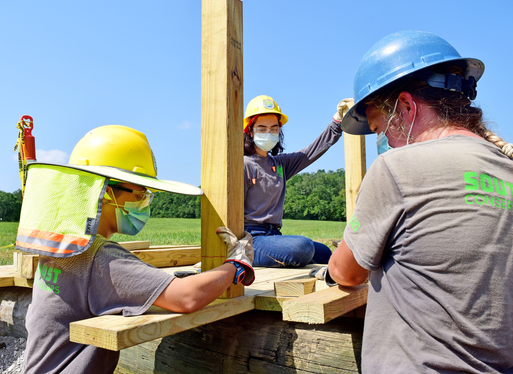 Staff Photo by Robin Rudd / From left, Southeast Conservation Corps team members Gracie Fogo, Autumn Riehl and Emily Mathis discuss the position of a post for a footbridge they're building across a stream in McDonald Field in Chickamauga and Chattanooga National Military Park.
