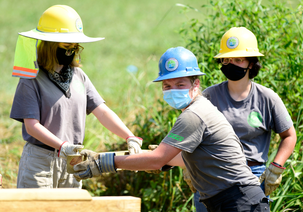 Staff Photo by Robin Rudd / From left, Southeast Conservation Corps team member Juliana Williams hands off a piece of lumber to Emily Mathis, as Ruth Beeland looks on. The crew is building a footbridge across a stream in McDonald Field, just south of Chickamauga and Chattanooga National Military Park's visitor center.