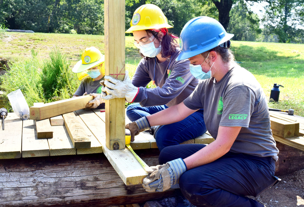 Staff Photo by Robin Rudd / From left, Southeast Conservation Corps team members Gracie Fogo, Autumn Riehl and Emily Mathis install posts on a bridge the team is building across a stream in McDonald Field near the Chickamauga and Chattanooga National Military Park's visitor center. n.