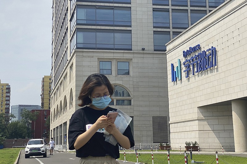 FILE - A woman uses her phone as she passes by the ByteDance headquarters in Beijing, China, on Friday, Aug. 7, 2020. The Chinese government is complicating the U.S.-government-ordered sale of U.S. TikTok assets. China on Friday, Aug. 28, 2020 introduced export restrictions on artificial intelligence technology, seemingly including the type that TikTok uses to choose which videos to spool up to its users. That means TikTok's Chinese owner, ByteDance, would have to obtain a license to export any restricted technologies to a foreign company. (AP Photo/Ng Han Guan)