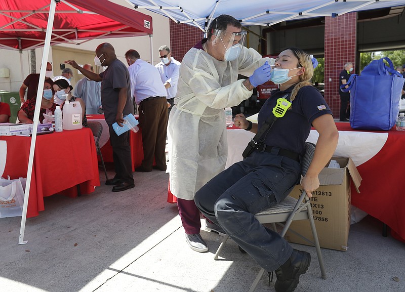 In this Aug. 6, 2020, file photo, Hialeah Fire Department Firefighter-Paramedic Laura Nemoga, right, winces as medical assistant Jesus Vera performs a COVID-19 test at Hialeah Fire Station #1, in Hialeah, Fla. The torrid coronavirus summer across the Sun Belt is easing after two disastrous months that brought more than 35,000 deaths. (AP Photo/Wilfredo Lee, File)