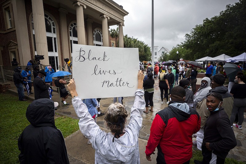 In this Thursday, June 4, 2020, file photo, a group of protesters gather outside the Glynn County Courthouse while a preliminary hearing is being held inside for Travis McMichael, Gregory McMichael and William Bryan, in Brunswick, Ga. The three are accused of shooting of Ahmaud Arbery while he ran through their neighborhood in February. The Glynn County commissioners are suing to stop a referendum on abolishing the county police department. State lawmakers approved the binding referendum in the spring after the February shooting death of Arbery. (AP Photo/Stephen B. Morton, File)