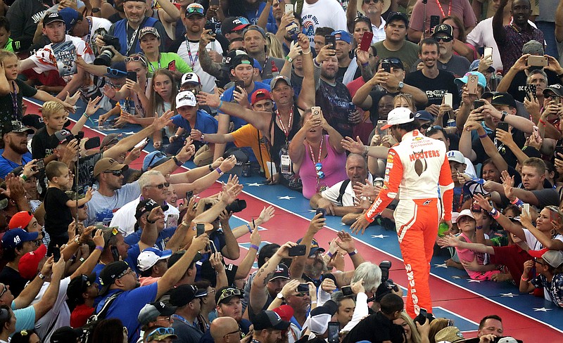 AP photo by John Raoux / NASCAR fans reach out to high-five Hendrick Motorsports driver Chase Elliott during introductions for a Cup Series race on July 7, 2018, at Daytona International Speedway. The access NASCAR provides fans to its stars has been lost since the series resumed racing amid the coronavirus pandemic, and that's not likely to change soon.