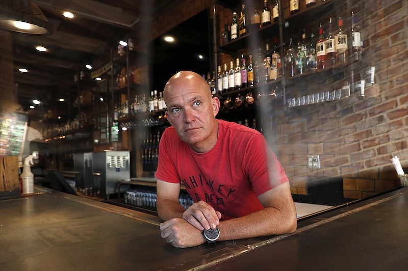 Jeff Brightwell, owner of Dot's Hop House, is framed between protective shielding placed over the bar as he poses for a photo at his establishment in the Deep Ellum entertainment district in Dallas, Thursday, Aug. 20, 2020. (AP Photo/Tony Gutierrez)
