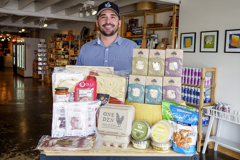 Staff photo by C.B. Schmelter / Owner Jesse Watlington poses with some of the new grocery offerings at Bleu Fox Cheese Shop.