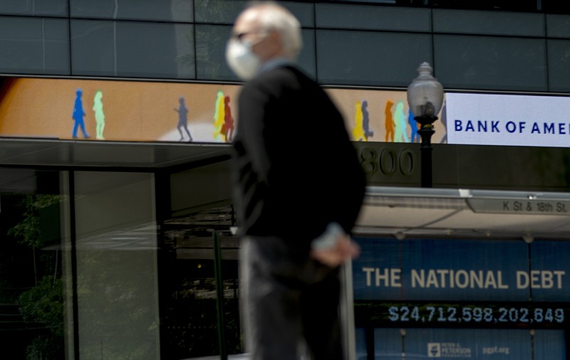 In this April 29, 2020 file photo, a man wearing a mask to protect against coronavirus, waits to cross the street as a digital sign displays groups of people walking above another sign displaying the size of the national debt along an empty K Street in Washington. The U.S. budget deficit hit an all-time high of $3 trillion for the first 11 months of this budget year, the Treasury Department said Friday, Sept. 11. (AP Photo/Andrew Harnik, File)