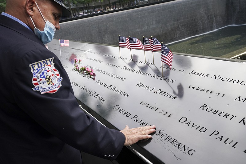 A mourner brushes water with his fingers over the name cut-outs of the deceased at the National September 11 Memorial and Museum, Friday, Sept. 11, 2020, in New York. (AP Photo/John Minchillo)