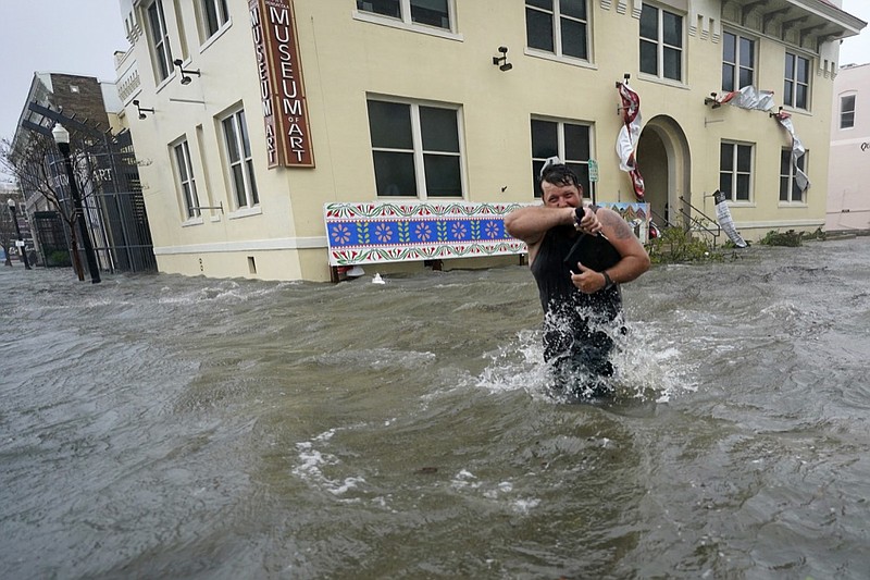 Trent Airhart wades through flood waters, Wednesday, Sept. 16, 2020, in downtown Pensacola, Fla. Hurricane Sally made landfall Wednesday near Gulf Shores, Alabama, as a Category 2 storm, pushing a surge of ocean water onto the coast and dumping torrential rain that forecasters said would cause dangerous flooding from the Florida Panhandle to Mississippi and well inland in the days ahead.(AP Photo/Gerald Herbert)