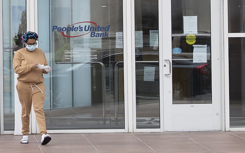 In this April 27, 2020 file photo, A\a woman wearing a face mask to protect against the coronavirus takes off disposable gloves after using an ATM at the People's United Bank on Main Street in downtown in Bridgeport, Conn. As bank branches remain shuttered, more people are having a go at doing their banking online. (AP Photo/Mary Altaffer, File)