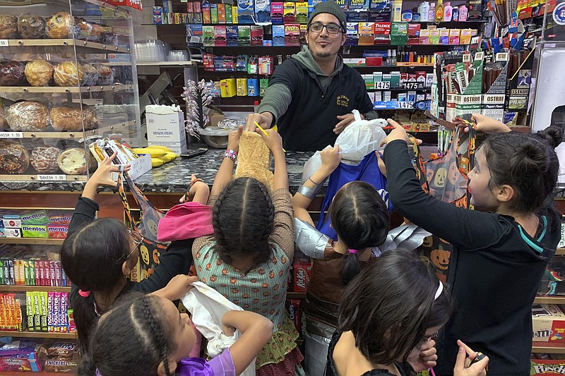 FILE - In this Oct. 31, 2018 file photo, a local convenient store worker, hands out candy to trick or treaters on Halloween in Brooklyn Borough of New York. U.S. sales of Halloween candy were up 13% over last year in the month ending Sept. 6, 2020 according to data from market research firm IRI and the National Confectioners Association. (AP Photo/Wong Maye-E)