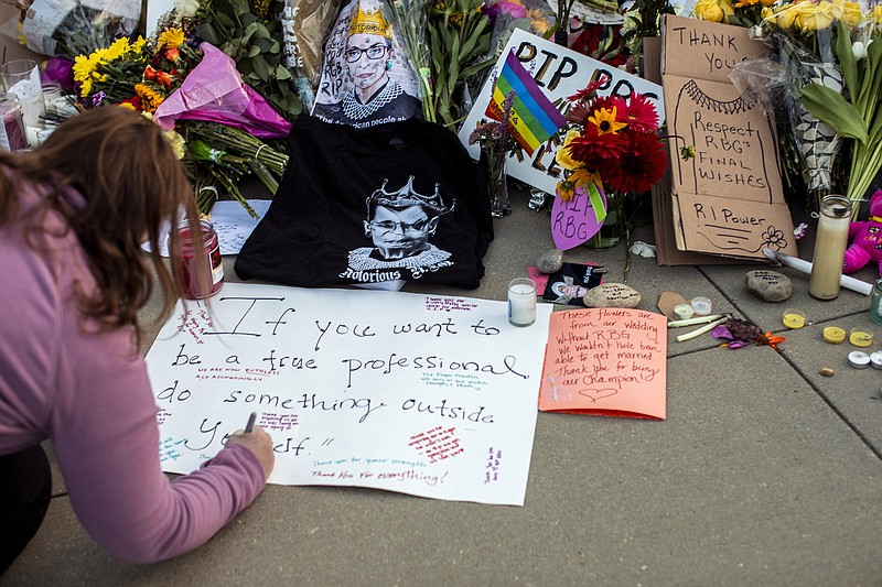 Photo by Jason Andrew of The New York Times / A mourner writes a message on a sign placed at a makeshift memorial outside the Supreme Court building in Washington on Saturday, Sept. 19, 2020, following the death of Justice Ruth Bader Ginsburg a day earlier.