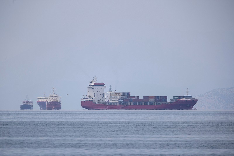 A cargo ship approaches the port of Piraeus as other ships are anchored, near Athens, Greece in this May 26, 2020 file photo. The United Nations is trying to figure out how to help more than 300,000 merchant mariners trapped at sea because of COVID-19 virus restrictions that they face when they get home. Describing the desperation of seafarers who've been afloat for a year or more, Captain Hedi Marzougui pleaded their case Thursday, Sept. 24, 2020 at a U.N.-organized meeting with shipping executives and government transport officials.(AP Photo/Petros Giannakouris, File)