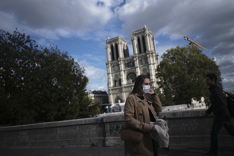 A woman walks by Notre Dame cathedral Saturday Sept.26, 2020 in Paris. While France suffered testing shortages early in the pandemic, ramped-up testing since this summer has helped authorities track a rising tide of infections across the country. More than 15,000 new cases were reported Friday, and the Paris hospital system is starting to delay some non-virus surgeries to free up space for COVID-19 patients. (AP Photo/Lewis Joly)