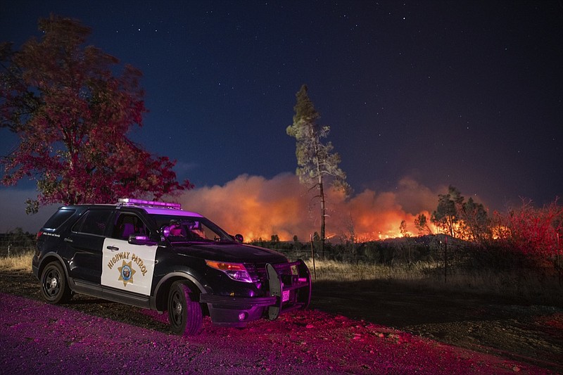 A California Highway Patrol officer watches flames that are visible from the Zogg Fire on Clear Creek Road near Igo, Calif., on Monday, Sep. 28, 2020. (AP Photo/Ethan Swope)