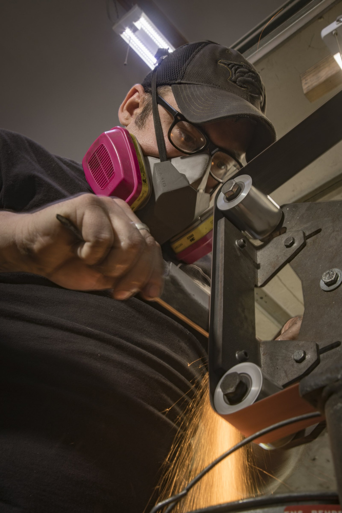 Staff photo by Troy Stolt / Mak Kelsay, owner and operator of 6Ear Knife and Tool uses a belt sander to profile a kitchen knife inside of Kelsay's home, where he has a shop in his garage Friday, Oct. 2, 2020 in Ooltewah, Tenn.