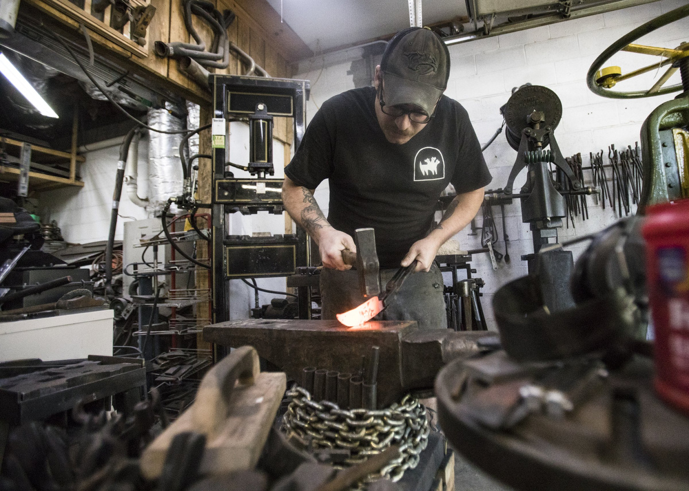 Staff photo by Troy Stolt / Mak Kelsay, owner and operator of 6ear Knife and Tool works to draw out a piece of steel into a kitchen knife with a hammer inside of Kelsay's home, where he has a shop in his garage on Friday, Oct. 2, 2020 in Ooltewah, Tenn.