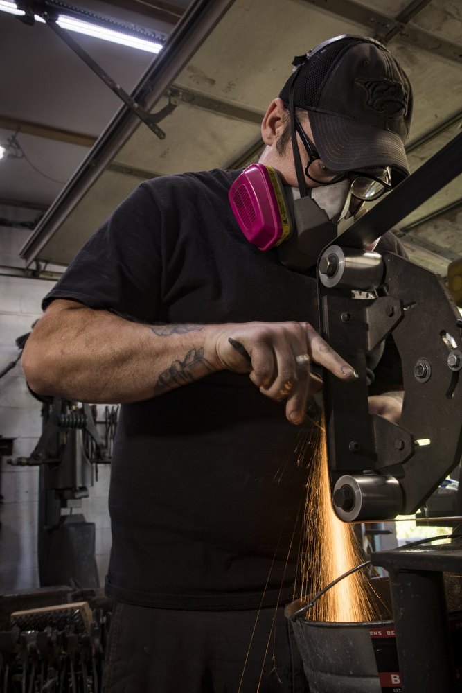 Staff photo by Troy Stolt / Mak Kelsay, owner and operator of 6Ear Knife and Tool uses a belt sander to profile a kitchen knife inside of Kelsay's home, where he has a shop in his garage Friday, Oct. 2, 2020 in Ooltewah, Tenn.