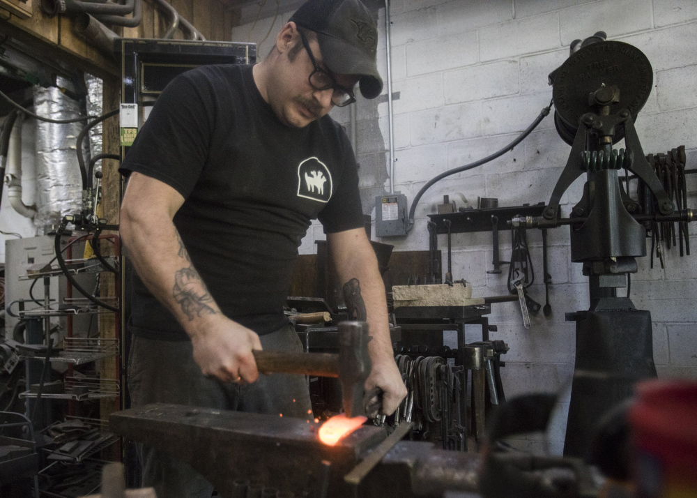 Staff photo by Troy Stolt / Mak Kelsay, owner and operator of 6Ear Knife and Tool hammers a red hot piece of steel into the shape of a kitchen knife inside of Kelsay's home, where he has a shop in his garage on Friday, Oct. 2, 2020 in Ooltewah, Tenn.