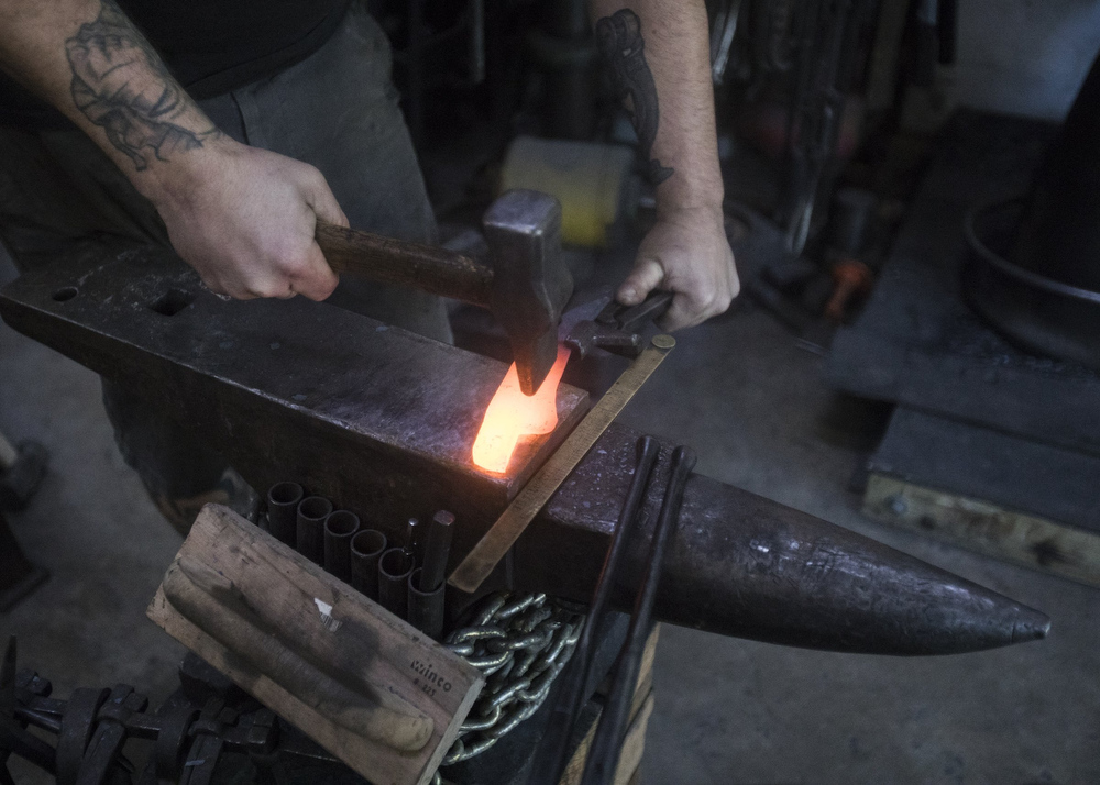 Staff photo by Troy Stolt / Mak Kelsay, owner and operator of 6Ear Knife and Tool hammers a red hot piece of steel into the shape of a kitchen knife inside of Kelsay's home, where he has a shop in his garage on Friday, Oct. 2, 2020 in Ooltewah, Tenn.