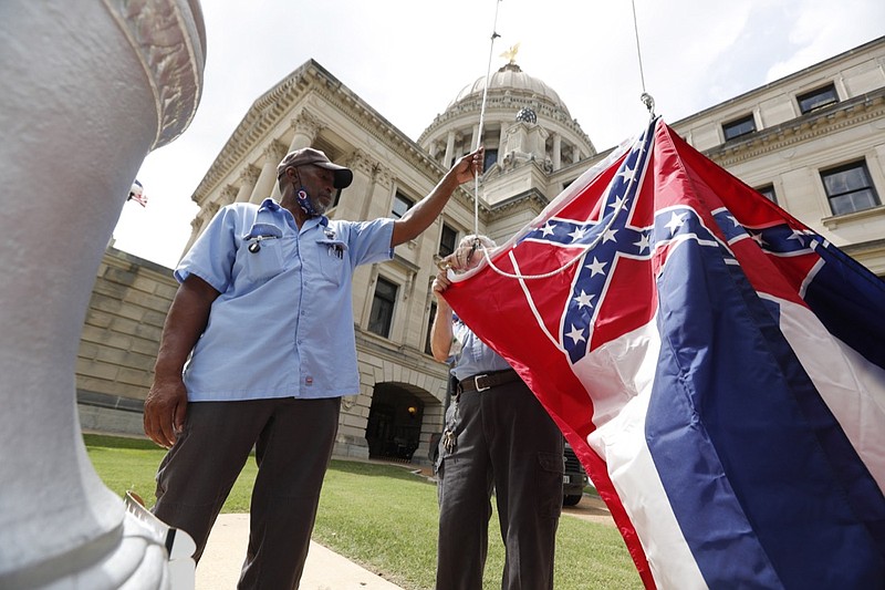 FILE - In this Tuesday, June 30, 2020 file photo, Mississippi Department of Finance and Administration employees Willie Townsend, left, and Joe Brown, attach a Mississippi state flag to the harness before raising it over the Capitol grounds in Jackson, Miss. State legislators voted in June to retire the last state flag in the U.S. bearing the Confederate battle emblem, and voters will decide on Nov. 3, 2020 whether to accept a new flag with a magnolia design. (AP Photo/Rogelio V. Solis)