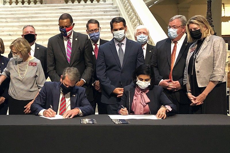 Georgia Gov. Brian Kemp, left, and Centers for Medicare and Medicaid Services Administrator Seema Verma sign health care waivers at the state Capitol in Atlanta, Thursday, Oct. 15, 2020. Georgia's plans would provide Medicaid access to adults who make less than poverty level incomes who meet work requirements, and leave private brokers as the only avenue to buy federally-subsidized private insurance for people with above-poverty incomes. (AP Photo/Jeff Amy)