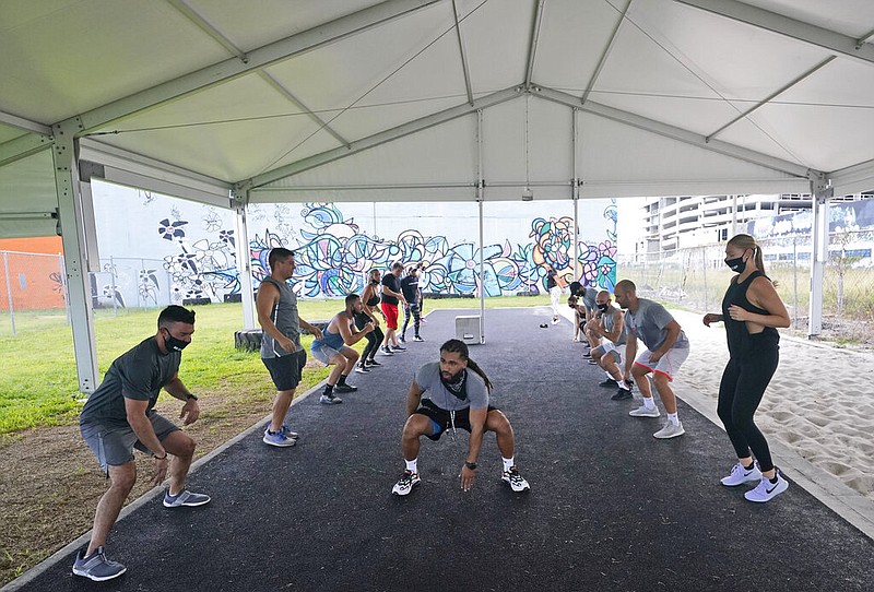 Trainer Legend Tarvers, center, leads a group during a workout at Legacy Fit, Monday, Aug. 31, 2020, in Miami. As the vast majority of in-person fitness clubs switched to virtual classes when the pandemic hit, Legacy Fit took the opposite approach. When Florida became one of the nation's COVID-19 hot spots in July, CEO Manning Sumner decided to host classes in a ballroom-sized outdoor tent that would still ensure safety, but allow clients to exercise in-person. (AP Photo/Wilfredo Lee)