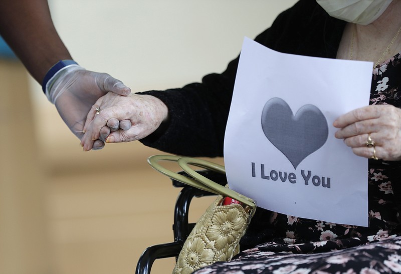 In this July 17, 2020 file photo, a senior citizen holds the hand of a care coordinator at a Health facility in Miami. Federal health officials on Friday unveiled a plan to get approved coronavirus vaccines to nursing home residents free of cost, with the aid of two national pharmacy chains.No vaccine has yet been approved by the Food and Drug Administration, and the distribution program is contingent on that happening first. (AP Photo/Wilfredo Lee)