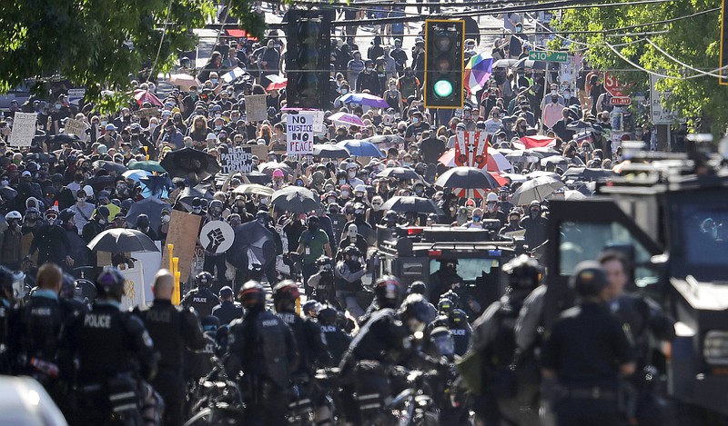 In this July 25, 2020, file photo, police clash with protesters during a Black Lives Matter protest near the Seattle Police East Precinct headquarters in Seattle. New York, Seattle and Portland, three cities recently labeled "anarchist jurisdictions" by the U.S. Justice Department, are suing to to invalidate the designation and to fight off the Trump administration's efforts to withhold federal dollars. The lawsuit, filed Thursday, Oct. 22, 2020 in U.S. District Court in Seattle, ridiculed Trump's action as offensive to the Constitution and common sense, but said the consequences of withholding federal money during a pandemic "are deadly serious." (AP Photo/Ted S. Warren, File)