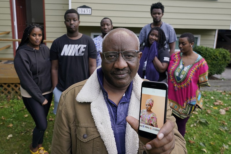 Sophonie Bizimana, center, a permanent U.S. resident who is a refugee from Congo, poses for a photo, Wednesday, Oct. 14, 2020, at his home in Kirkland, Wash., along with six of his children as he displays a cell-phone photo of his wife, Ziporah Nyirahimbya, who is in Uganda and has been unable so far to join him in the U.S. For decades, America admitted more refugees annually than all other countries combined, but that reputation has eroded during Donald Trump's presidency as he cut the number of refugees allowed in by more than 80 percent. (AP Photo/Ted S. Warren)
