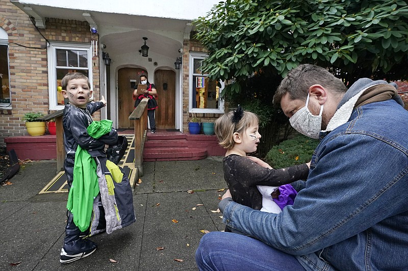 Alex Stonehill gets a goodbye from his daughter Helenore, 2, as her brother Malcolm, 4, motions to a friend arriving at the Community Day Center for Children on Thursday, Oct. 29, 2020, in Seattle. As more families make the jump back to group day care this fall in an attempt to restart lives and careers, many parents, pediatricians and care operators are finding that new, pandemic-driven rules offer a much-needed layer of safety but also seem incompatible with the germy reality of childhood. (AP Photo/Elaine Thompson)