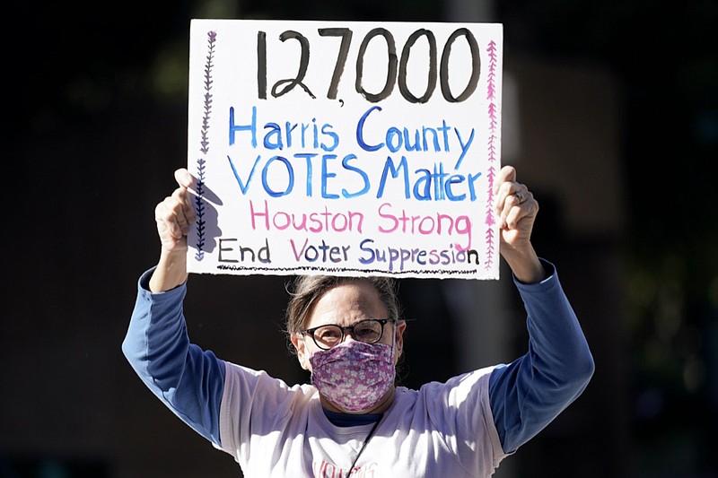 Demonstrator Gina Dusterhoft holds up a sign as she walks to join others standing across the street from the federal courthouse in Houston, Monday, Nov. 2, 2020, before a hearing in federal court involving drive-thru ballots cast in Harris County. The lawsuit was brought by conservative Texas activists, who have railed against expanded voting access in Harris County, in an effort to invalidate nearly 127,000 votes in Houston because the ballots were cast at drive-thru polling centers established during the pandemic. (AP Photo/David J. Phillip)