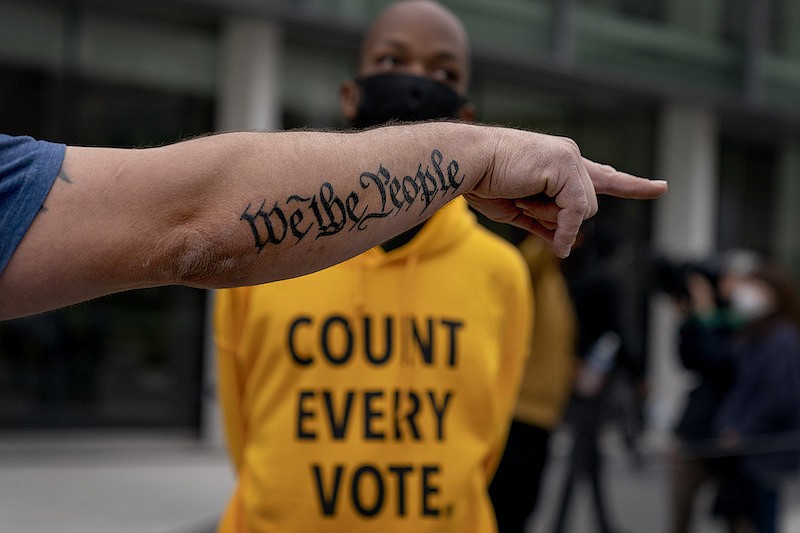 The tattoo "We The People", a phrase from the United States Constitution, decorates the arm of Trump supporter Bob Lewis, left, as he argues with counter protestor Ralph Gaines while Trump supporters demonstrate against the election results outside the central counting board at the tcf Center in Detroit, Thursday, Nov. 5, 2020. (AP Photo/David Goldman)