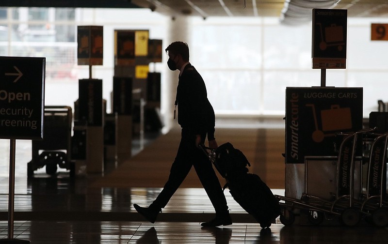 FILE - In this Thursday, April 9, 2020, file photo, a lone airline crew member pulls his bags behind him as he walks through the baggage-claim area at Denver International Airport in Denver, amid the coronavirus outbreak. (AP Photo/David Zalubowski, File)