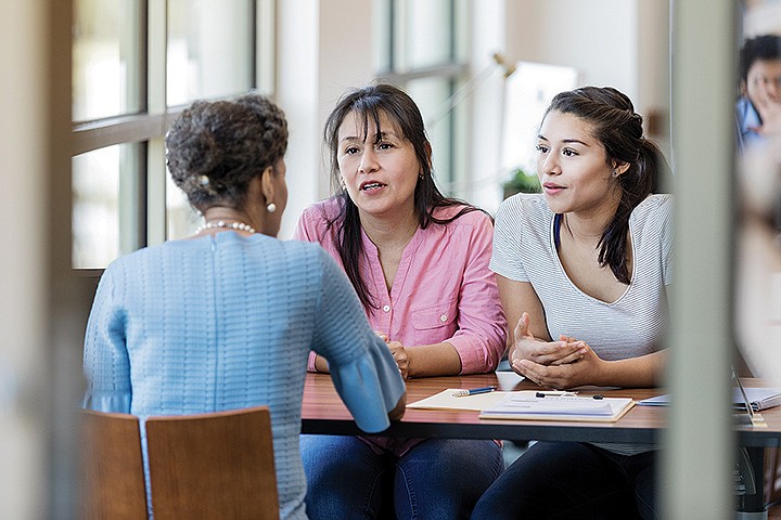 Hispanic woman and her young adult daughter talk with loan officer about a loan for college education. / Photo credit: Getty Images/iStock/SDI Productions