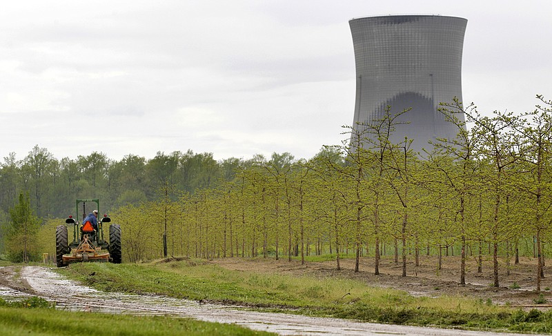 FILE - In this May 18, 2011, file photo, a worker is seen in the area surrounding a tree farm in North Perry, Ohio, near the two cooling towers of the Perry Nuclear Power Plant looming in the backgrouwnd. Amid intense scrutiny of the roles company officials played in an alleged $60 million bribery scheme to obtain a $1 billion bailout for two aging nuclear power plants, Ohio's largest electric utility has announced a goal to become "carbon neutral" by 2050 while reducing greenhouse gas emissions 30% by 2030. (AP Photo/Amy Sancetta, File)