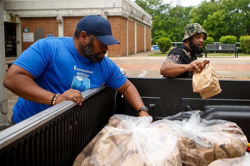 Staff photo by C.B. Schmelter / Troy Rogers, left, and Tony Oliver pass out bagged lunches on the Westside on Tuesday, May 5, 2020 in Chattanooga, Tenn.