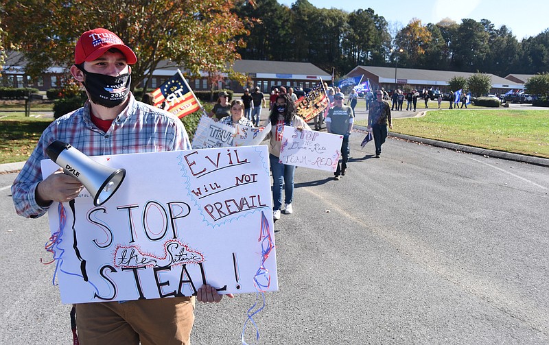 Staff Photo by Matt Hamilton / Chatsworth resident Seth Vineyard carries a sign as Trump supporters walk across a parking lot to the rally site on Saturday. The rally took place Saturday, Nov. 14, 2020 in Dalton at the intersection of Glenwood Ave. and Walnut Ave. 