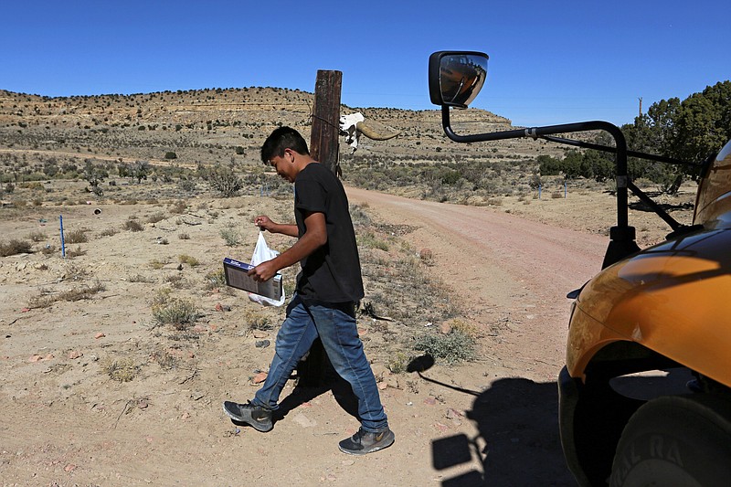 A student carries a math book delivered by school bus driver Kelly Maestas along his rural route outside Cuba, N.M., Oct. 19, 2020. The switch to remote learning in rural New Mexico has left some students profoundly isolated — cut off from others and the grid by sheer distance. The school system is sending school buses to students' far-flung homes to bring them assignments, meals and a little human contact. (AP Photo/Cedar Attanasio)
