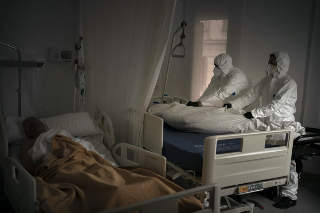 Wearing protective suits to avoid infection, funeral home workers remove the body of an elderly person who died of COVID-19 at a nursing home while another resident sleeps in his bed in Barcelona, Spain, on Nov. 5, 2020. (AP Photo/Emilio Morenatti)
