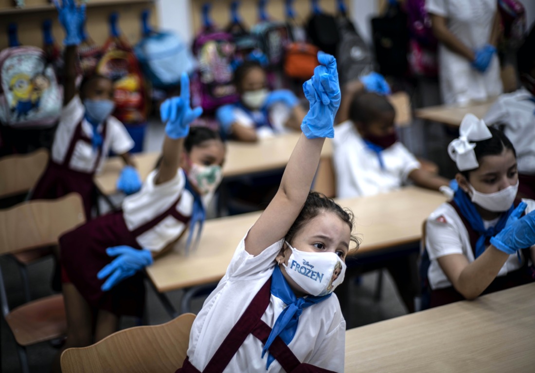 Wearing masks and plastic gloves to prevent the spread of the coronavirus, girls raise their hands during class in Havana, Cuba, on Monday, Nov. 2, 2020. Tens of thousands of school children returned to class Monday in Havana for the first time since April. (AP Photo/Ramon Espinosa)