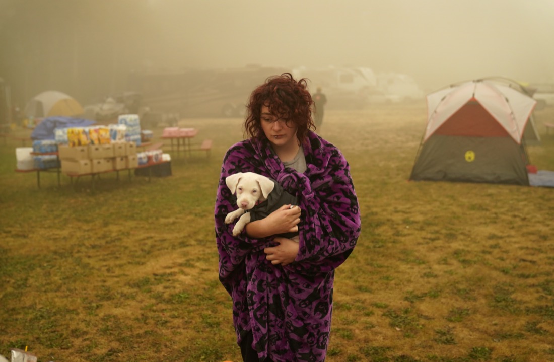 Shayanne Summers holds her dog Toph while wrapped in a blanket on Sept. 13, 2020, after staying several days in a tent at an evacuation center at the Milwaukie-Portland Elks Lodge in Oak Grove, Ore. Summers evacuated from near Molalla, Ore., which was threatened by the Riverside Fire. (AP Photo/John Locher)