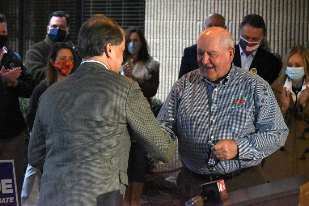 Staff Photo by Matt Hamilton / Jevin Jensen, chairman-elect of the Whitfield County Board of Commissioners, left, shakes hands with former Governor Sonny Perdue at the Dalton Municipal Airport on Monday, Dec. 14, 2020.