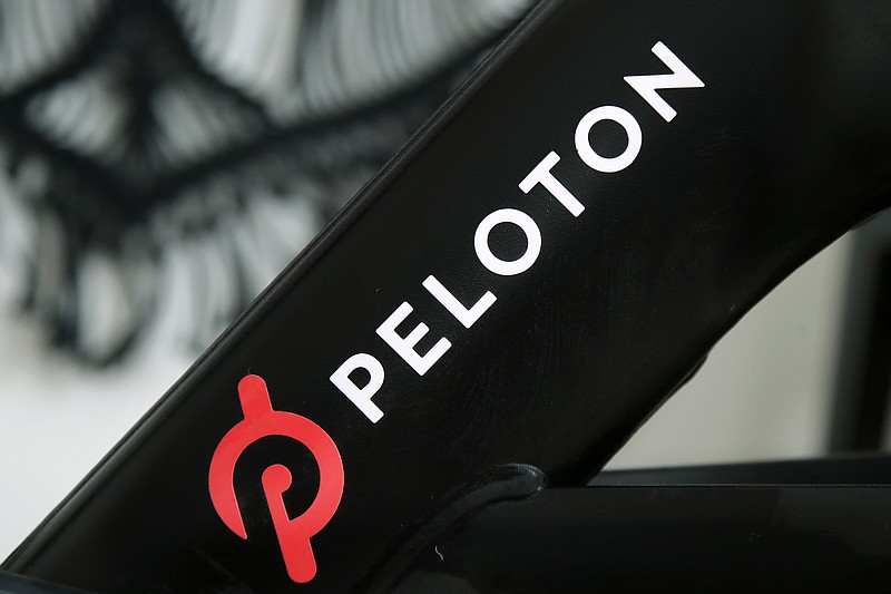 This Nov. 19, 2019, photo shows a Peloton logo on the company's stationary bicycle in San Francisco. Peloton is betting big that home workouts will continue to be popular next year and beyond, snapping up commercial exercise equipment maker Precor in a deal that will give Peloton its first manufacturing capacity in the U.S. Shares of Peloton jumped 13% in Tuesday, Dec. 21, 2020 trading, signaling investors like the move. (AP Photo/Jeff Chiu)