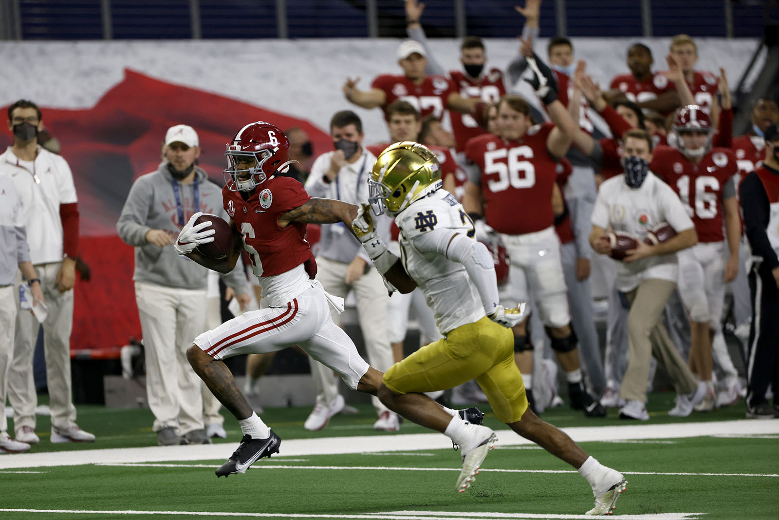 The Alabama sideline erupts in celebration as wide receiver DeVonta Smith (6) sprints to the end zone for a touchdown as Notre Dame safety Shaun Crawford (20) gives chase in the first half of the Rose Bowl NCAA college football game in Arlington, Texas, Friday, Jan. 1, 2021. (AP Photo/Ron Jenkins)