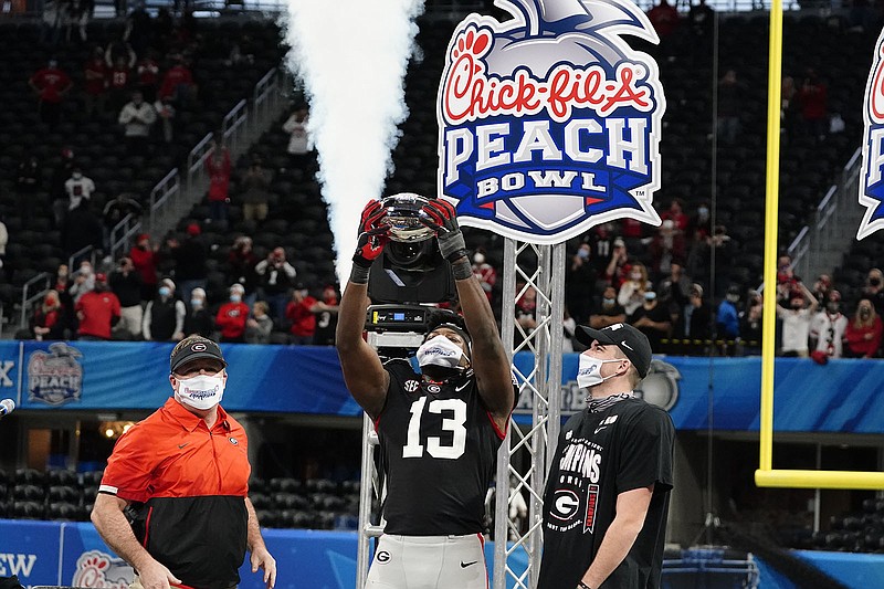 AP photo by Brynn Anderson / Georgia outside linebacker Azeez Ojulari holds up the Chick-fil-A Peach Bowl trophy as coach Kirby Smart and kicker Jack Podlesny look on Friday afternoon in Mercedes-Benz Stadium. Ojulari announced Saturday that he was forgoing his remaining eligibility with the Bulldogs.
