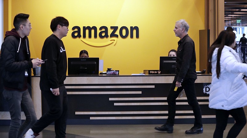 FILE - In this Nov. 13, 2018, file photo, employees walk through a lobby at Amazon's headquarters in Seattle. Amazon has announced $2 billion in loans and grants to secure affordable housing in three U.S. cities, including a Seattle suburb where the online retail giant employs at least 5,000 workers. Amazon said it would give $185.5 million to the King County Housing Authority to help buy affordable apartments in the region and keep the rents low, The Seattle Times reported Wednesday, Jan. 6, 2021. (AP Photo/Elaine Thompson)