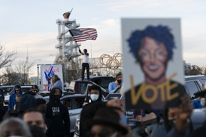 Photo by Carolyn Kaster of The Associated Press / People in the crowd hold up an image of Stacey Abrams and wave and American Flag as President-elect Joe Biden speaks in Atlanta on Monday, Jan. 4, 2021, to campaign for Georgia Democratic candidates for U.S. Senate, Rev. Raphael Warnock and Jon Ossoff.