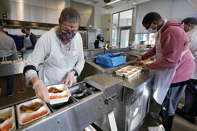 Volunteers Sheeran Howard, left, and Ibrahim Bahrr, right, package meals at Community Servings, which prepares and delivers scratch-made, medically tailored meals to individuals & families living with critical & chronic illnesses, Tuesday, Jan. 12, 2021, in the Jamaica Plain neighborhood of Boston. (AP Photo/Charles Krupa)



